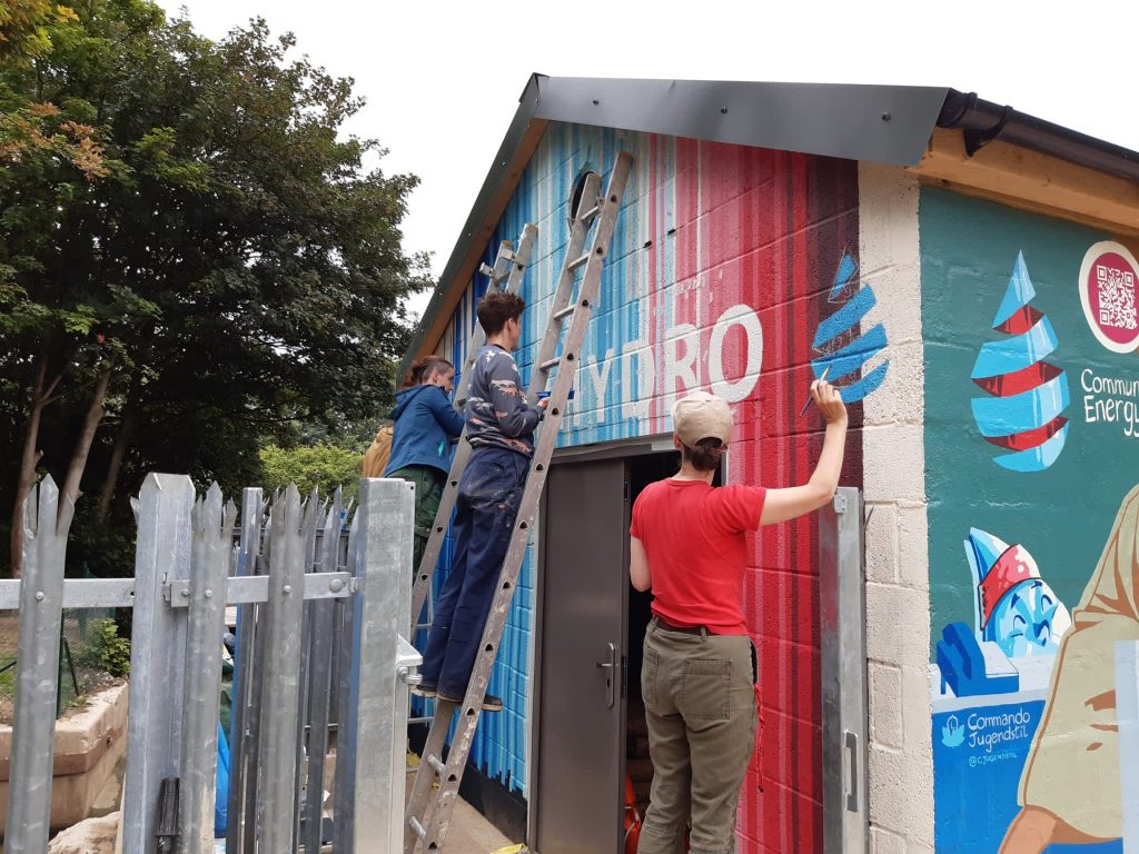 Three people standing, one of whom is on a ladder, painting a mural on the side of the Reading Hydro building