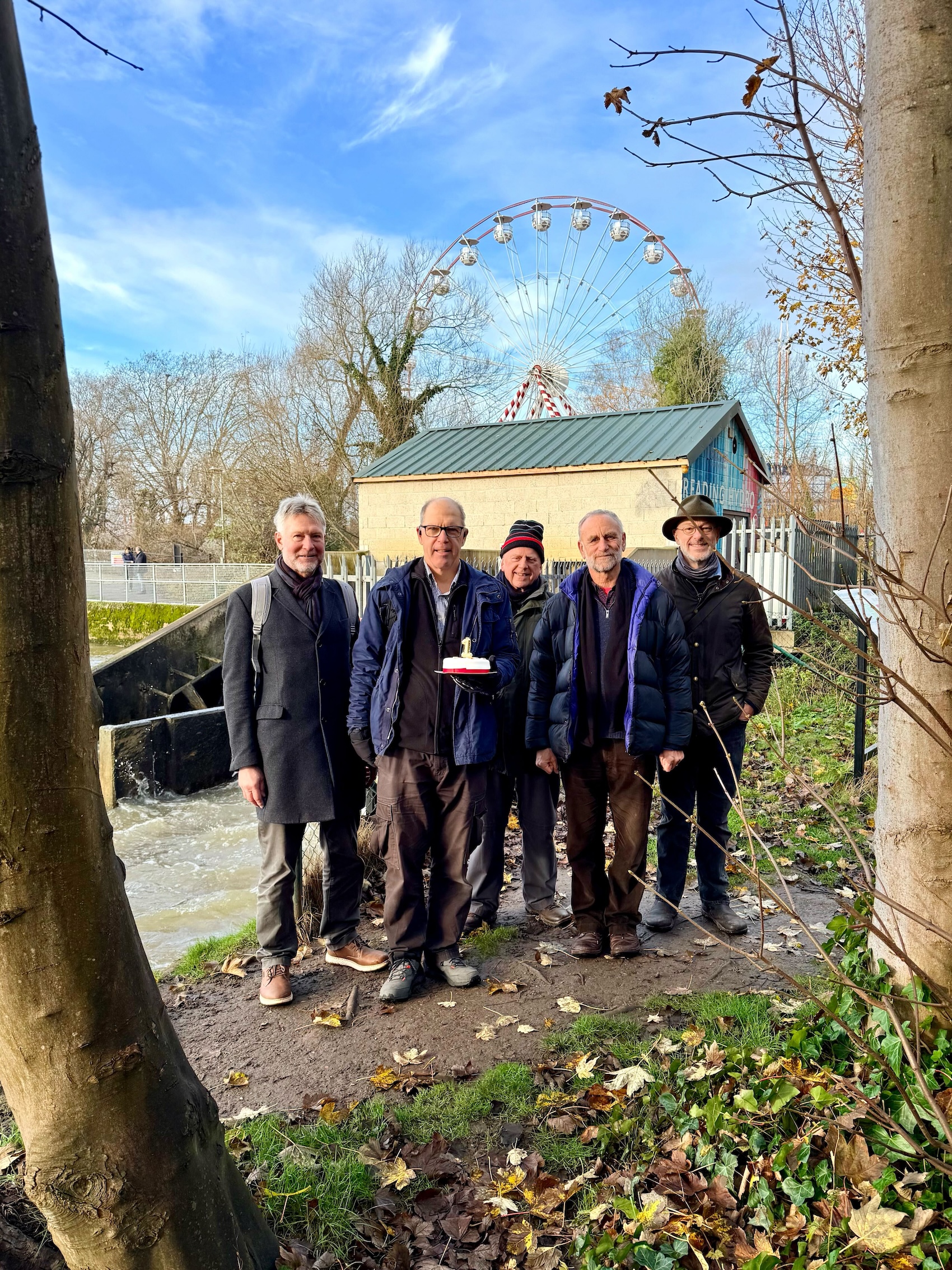 Hydro volunteers standing in front of the turbines holding a cake with a 1 candle