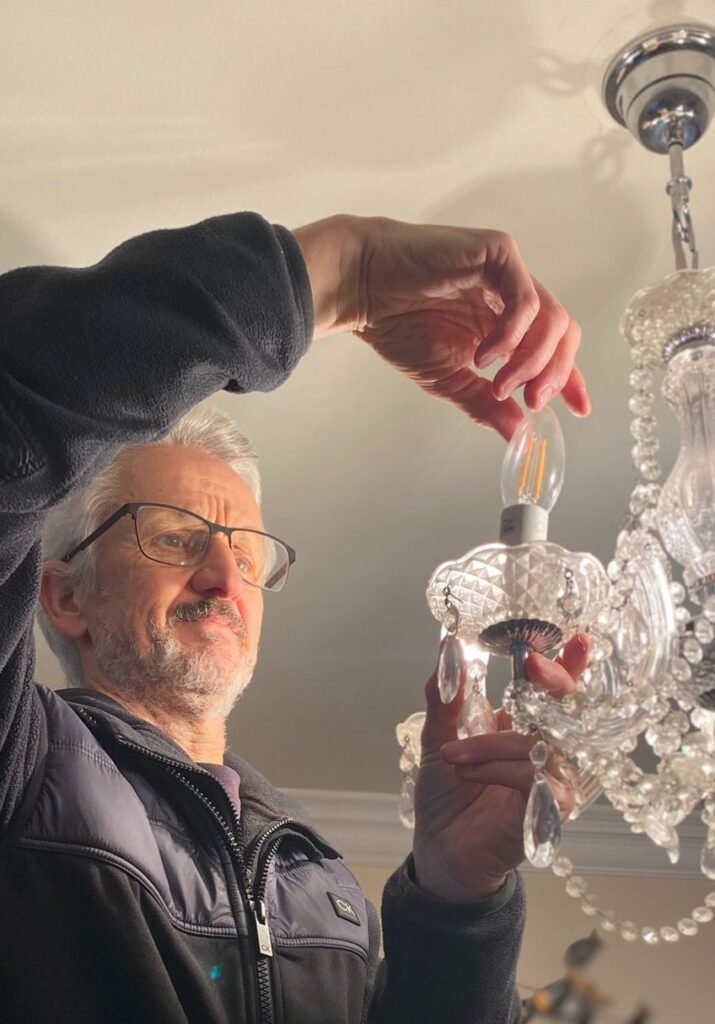 Man taking a candle bulb out of a chandelier light fitting